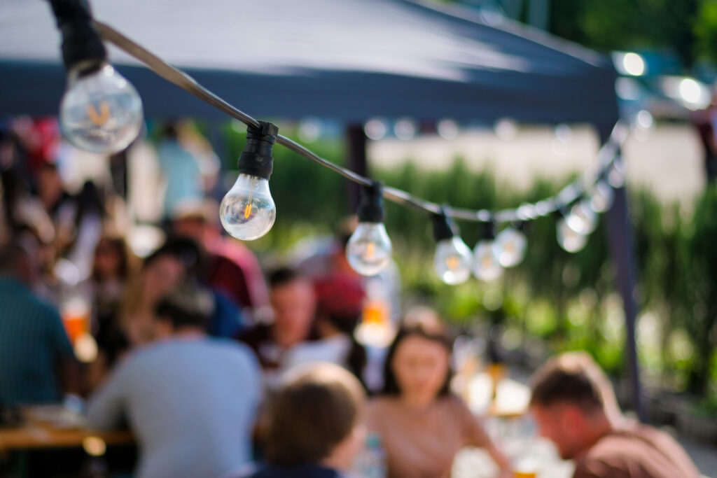 Hanged lamps at outdoor restaurant with multiple visitors on the background, BBQ,